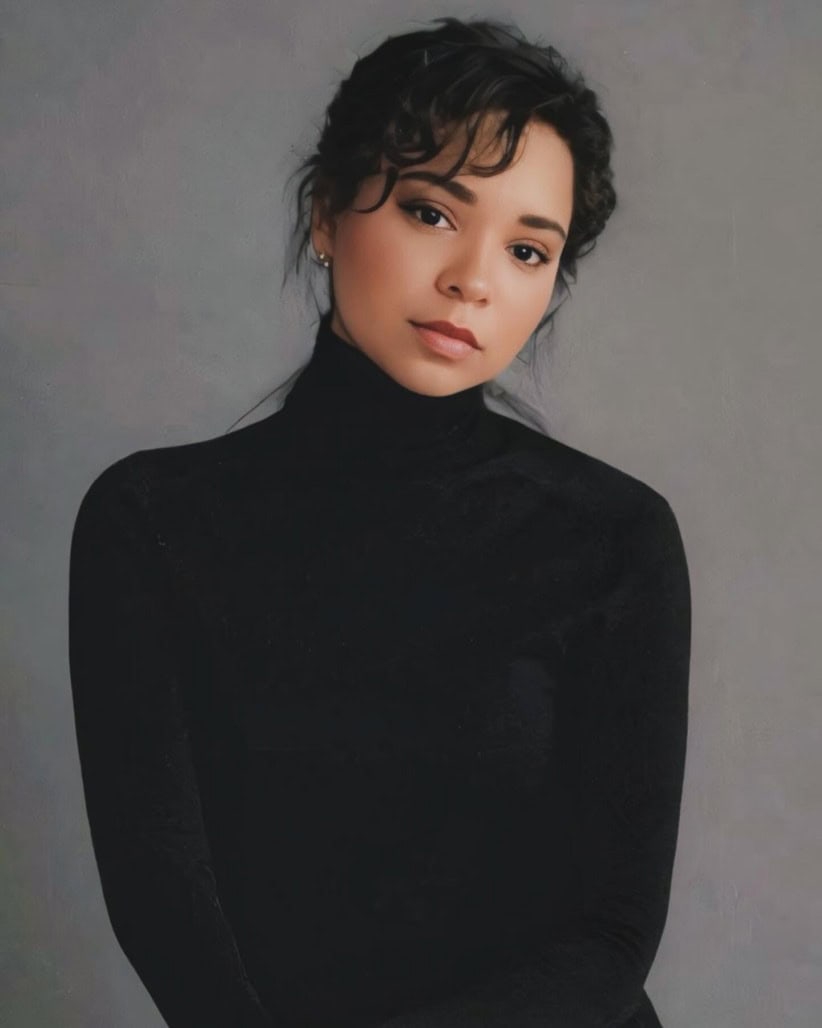 Portrait of a young woman with dark curly hair in a black turtleneck.