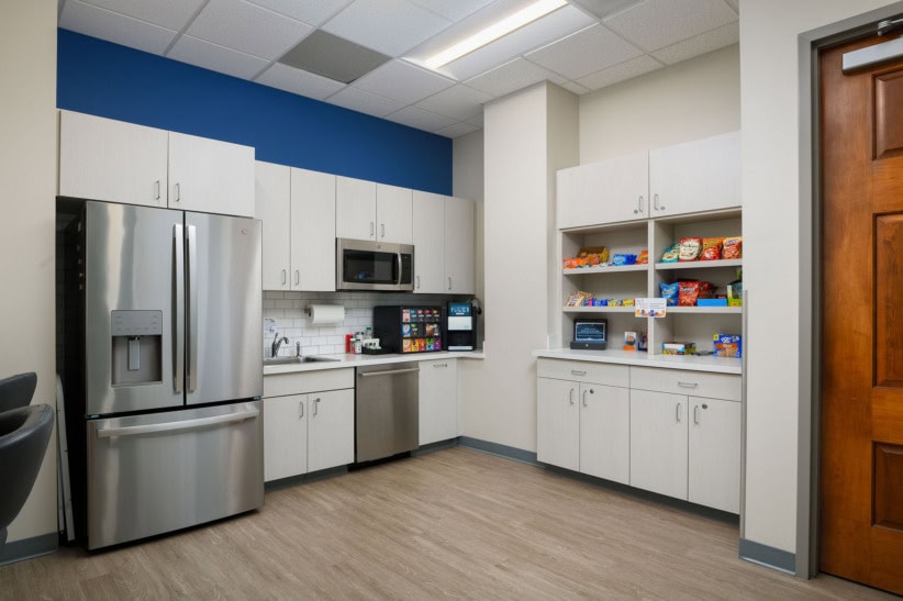 Modern office kitchenette with refrigerator, microwave, and snack shelves.