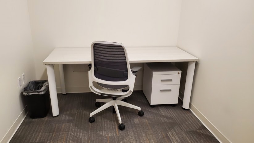 Modern office workspace with a white desk, black ergonomic chair, and small white drawer unit.