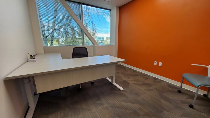 Modern office space with a white desk, black chair, and orange accent wall.