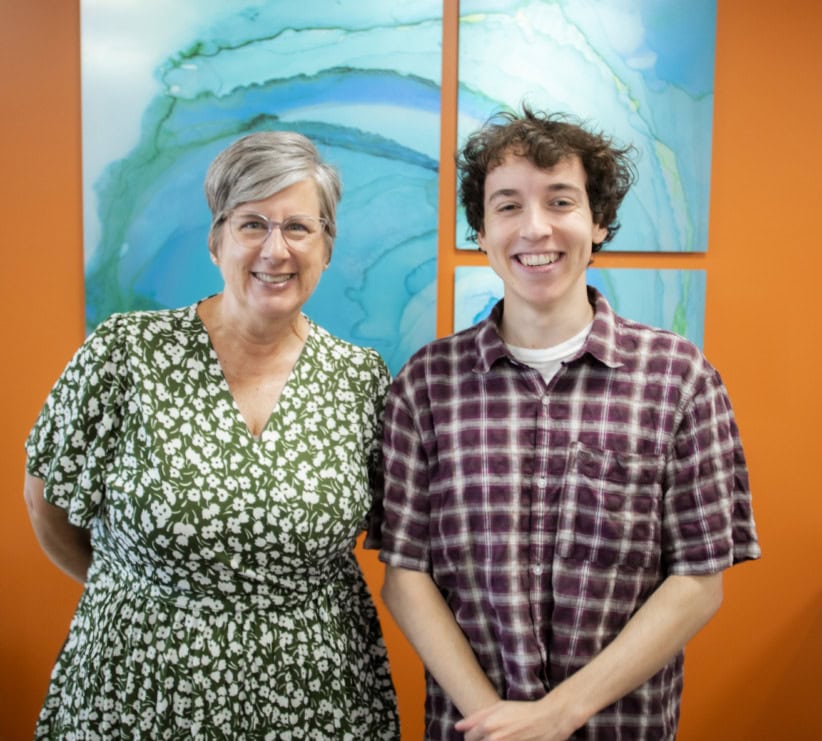 Smiling woman and young man in office setting with colorful abstract art.
