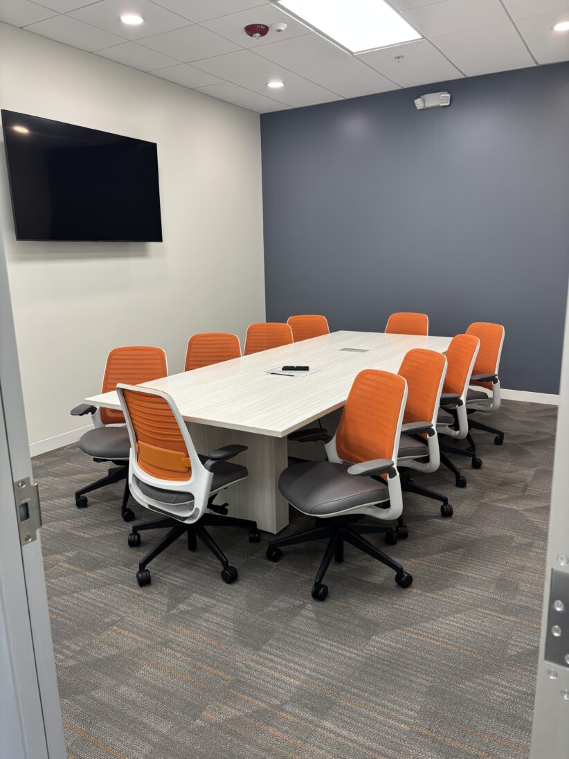 Modern conference room with orange ergonomic chairs, white table, wall-mounted TV, ideal for business meetings and coworking at Office Evolution.