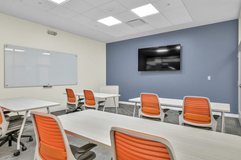 Modern coworking conference room with orange chairs and a large flat-screen TV at Office Evolution.