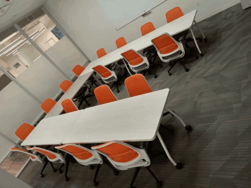 Modern conference room with white tables and orange chairs at Office Evolution.