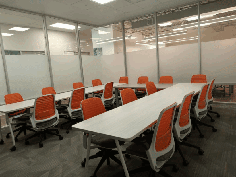 Modern office conference room with white tables and orange ergonomic chairs, ideal for collaborative meetings.