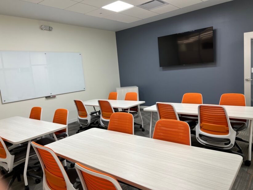 Modern office meeting room with white tables and orange chairs for collaborative work and client presentations.