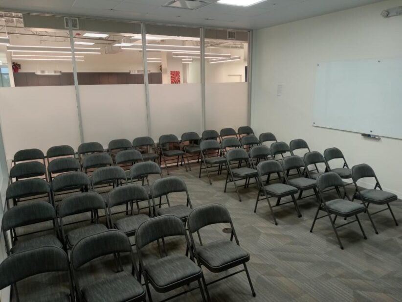 Spacious office meeting room with rows of black chairs, whiteboard, and modern workplace design.