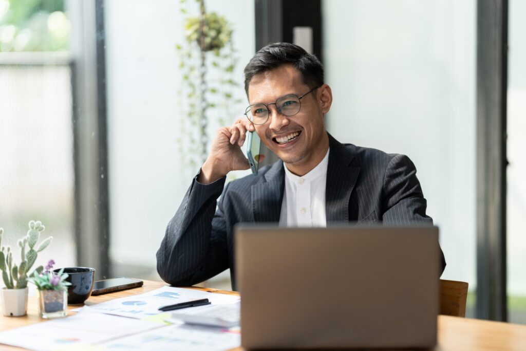 image of man with glasses sitting at office desk with is laptop, and he is talking on the phone
