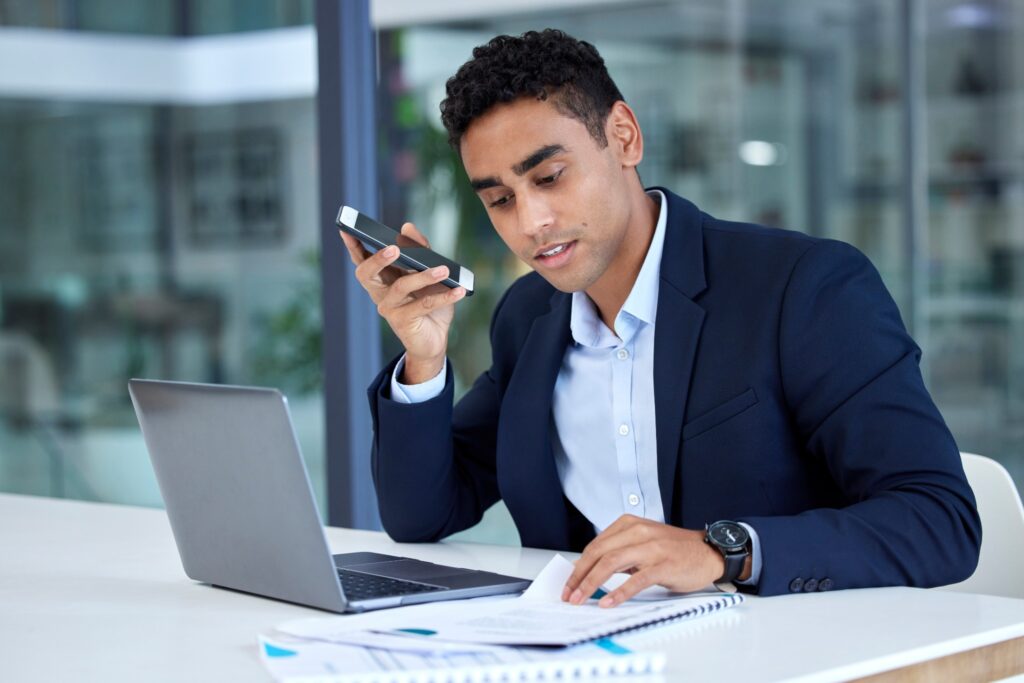 Image of young businessman at desk, having a conversation on speakerphone.