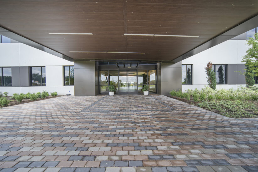 Modern office building entrance with landscaped surroundings and paved walkway.