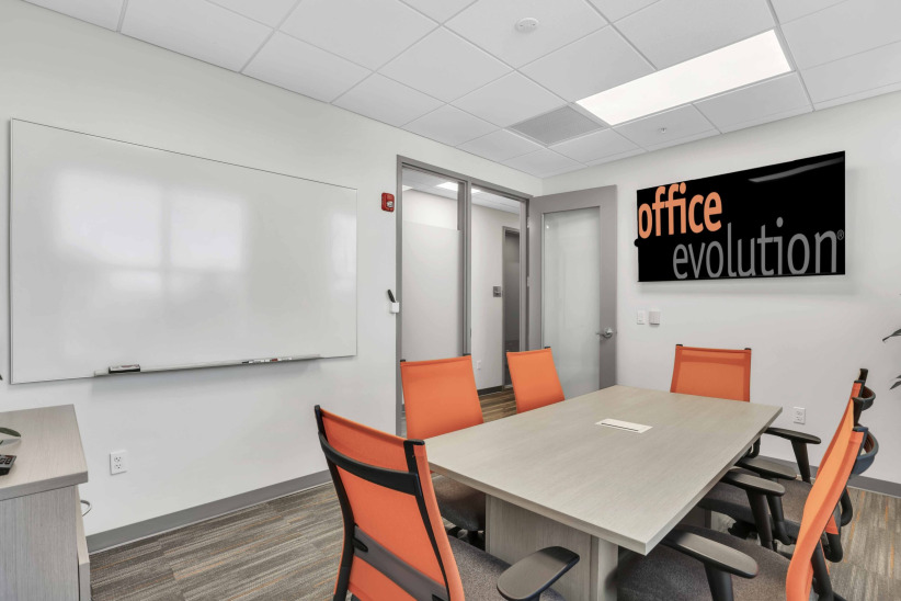 Modern office conference room with orange chairs, whiteboard, and Office Evolution sign.