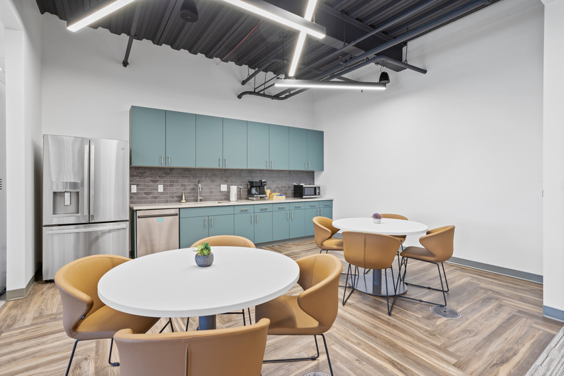 Modern office break room with kitchenette and seating area for remote work or meetings.