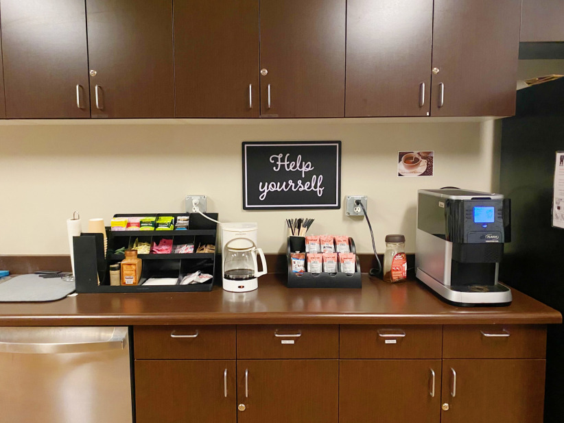 Office break area with coffee supplies and a sign saying "Help yourself" for coworking space amenities.