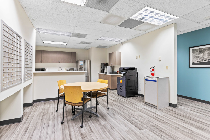 Modern office break room with seating, kitchen amenities, and printing station in a professional coworking space.