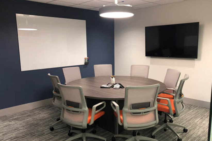 Office meeting room with a round table, ergonomic chairs, large screen TV, and modern office decor at Office Evolution.