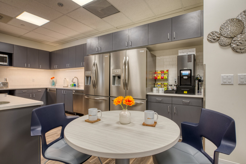 Modern office kitchen with stainless steel appliances and cozy seating area for employees.