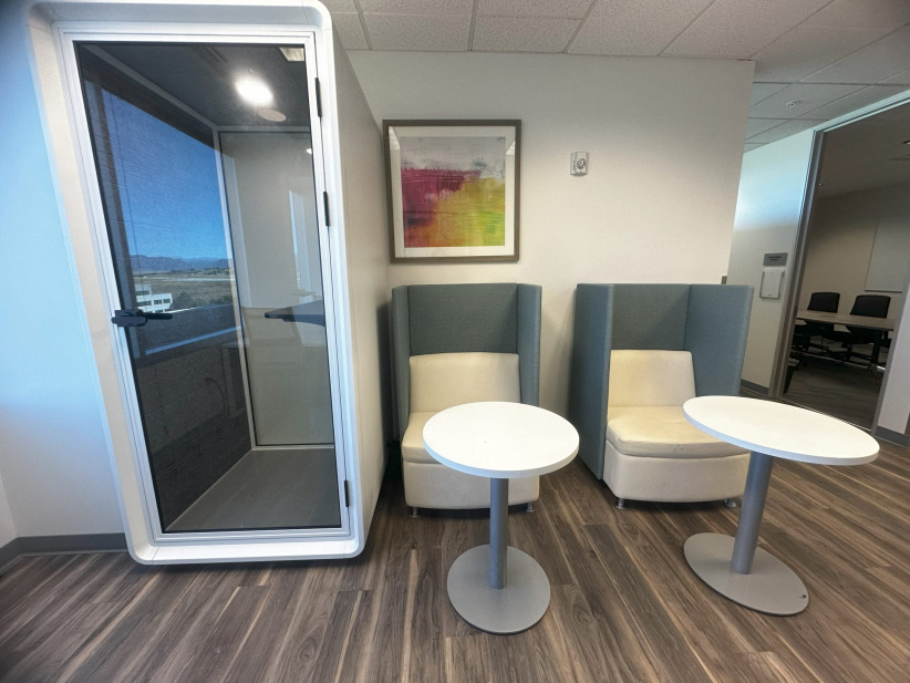 Modern office lounge with private enclosed phone booth, cozy seating, and contemporary decor, ideal for coworking spaces.
