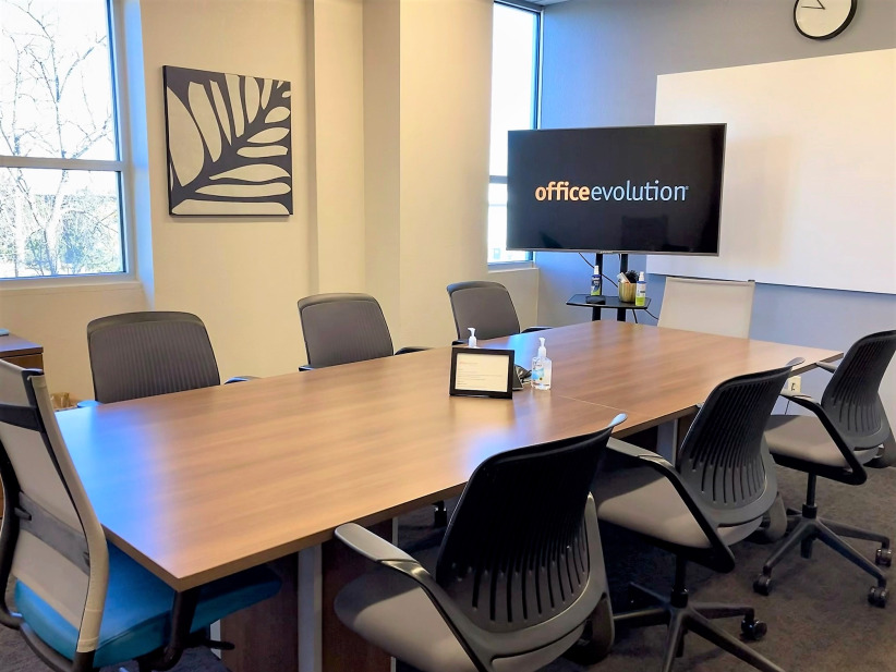 Office evolution conference room with modern furniture and large screen display for meetings; professional office space for remote work and collaboration.