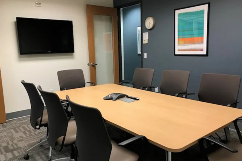Modern office conference room with a large table, chairs, and a wall-mounted TV for meetings and collaborations.
