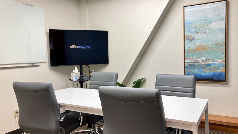 Modern office conference room with a white table, gray chairs, and a large screen for meetings and presentations.