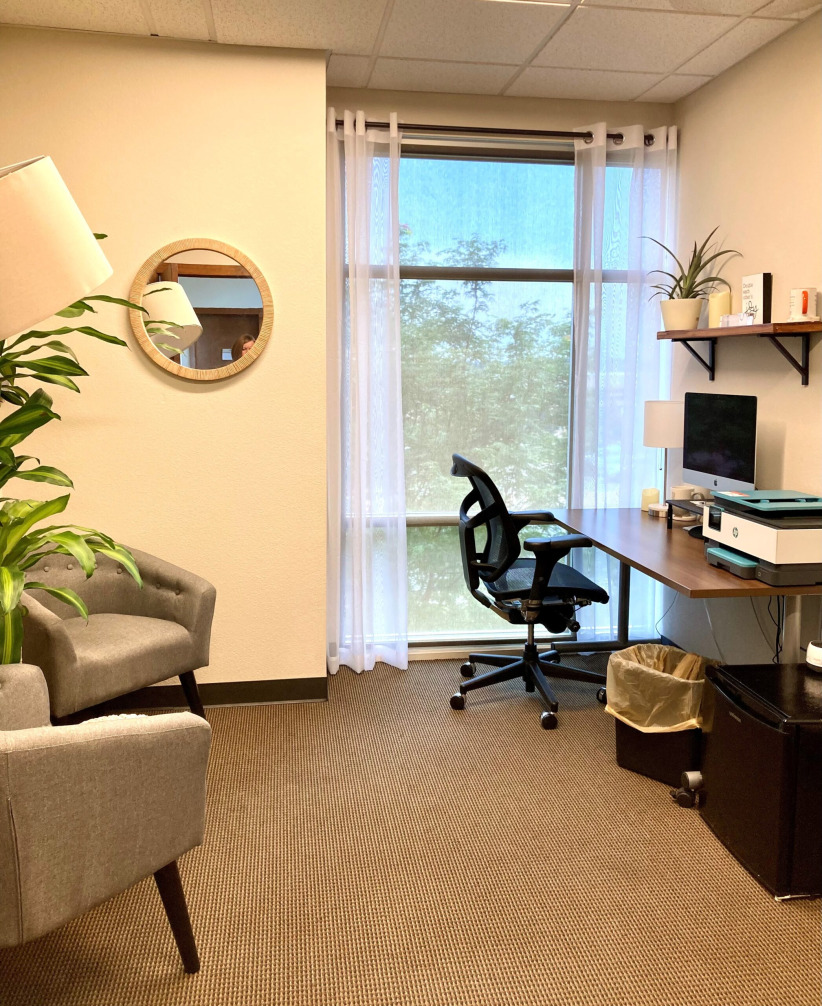 Modern office workspace with desk, chair, computer, and natural light from large window for productive work environment.
