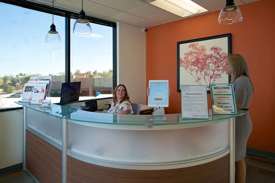 Professional office reception desk at Office Evolution with friendly staff, modern decor, and visitor sign-in station.