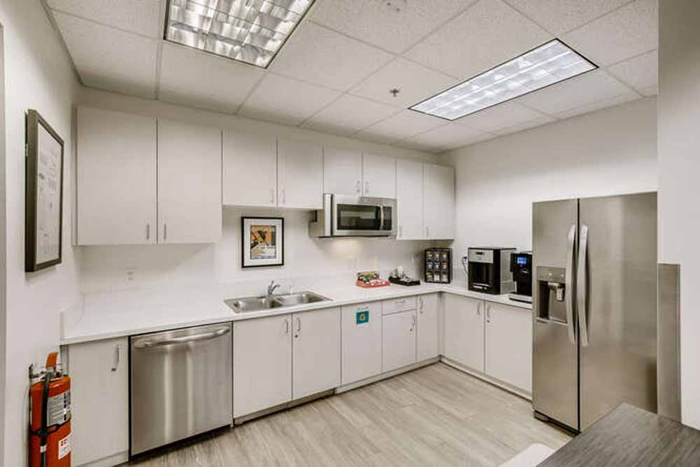 Modern office break room with stainless steel appliances and white cabinetry in a coworking space.