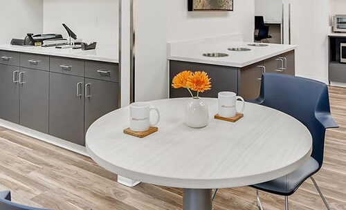 Modern office break area with a round table, flowers, and seating at Office Evolution.