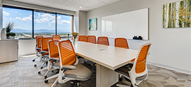 Modern office conference room with orange chairs and large windows providing natural light.