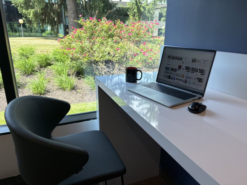 Modern office workspace with laptop and coffee mug near large window with garden view.
