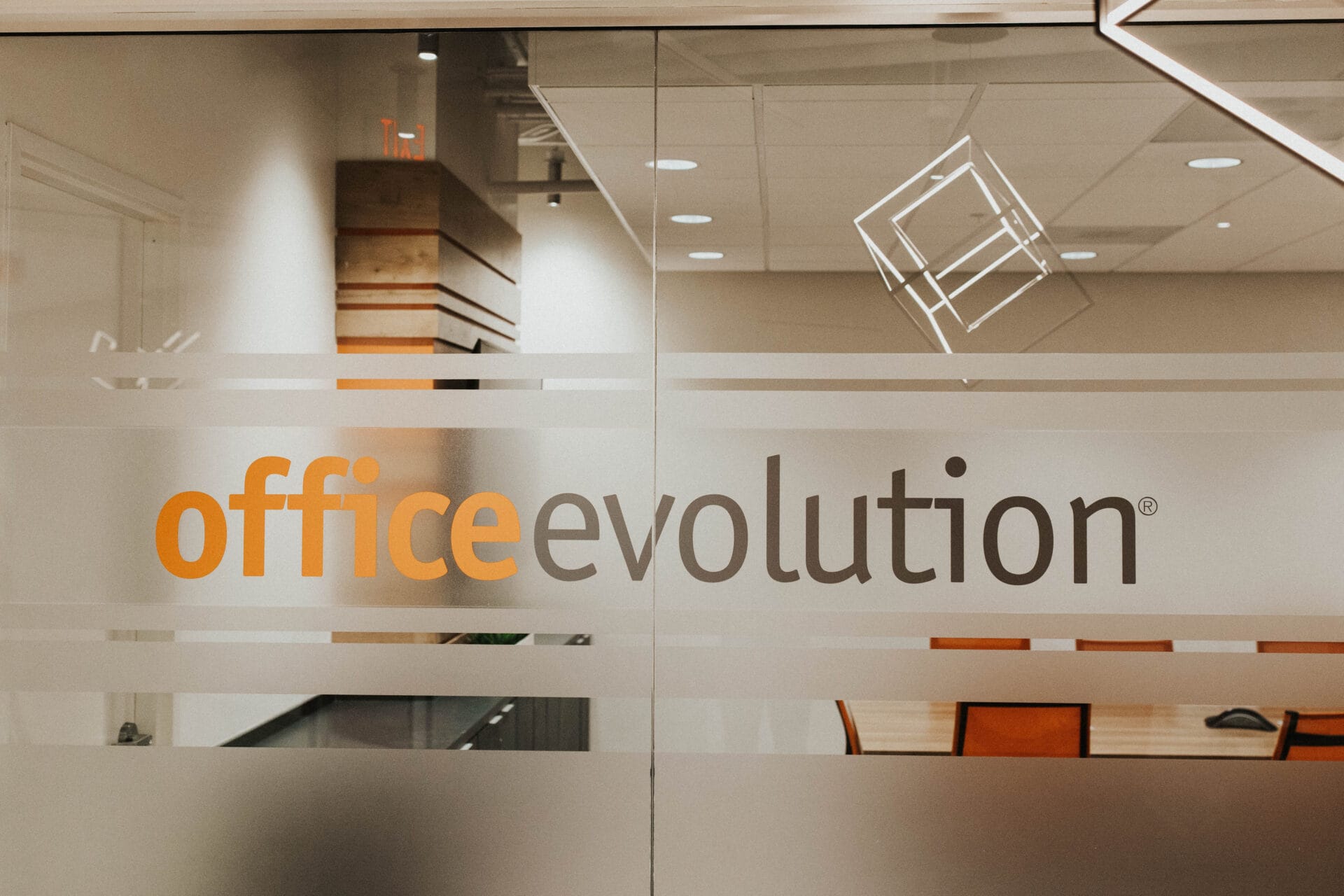 Modern office reception area at Office Evolution with glass doors and contemporary lighting | Professional office space at Office Evolution featuring glass doors and modern design | Interior view of Office Evolution workspace showcasing glass doors, logo, and modern office decor for professional business environments.