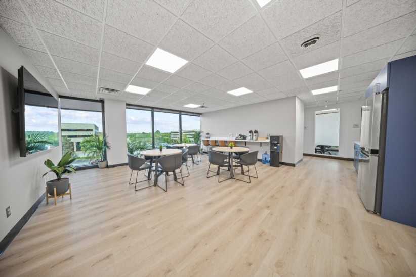 Modern office space with large windows, seating area, and kitchenette.
