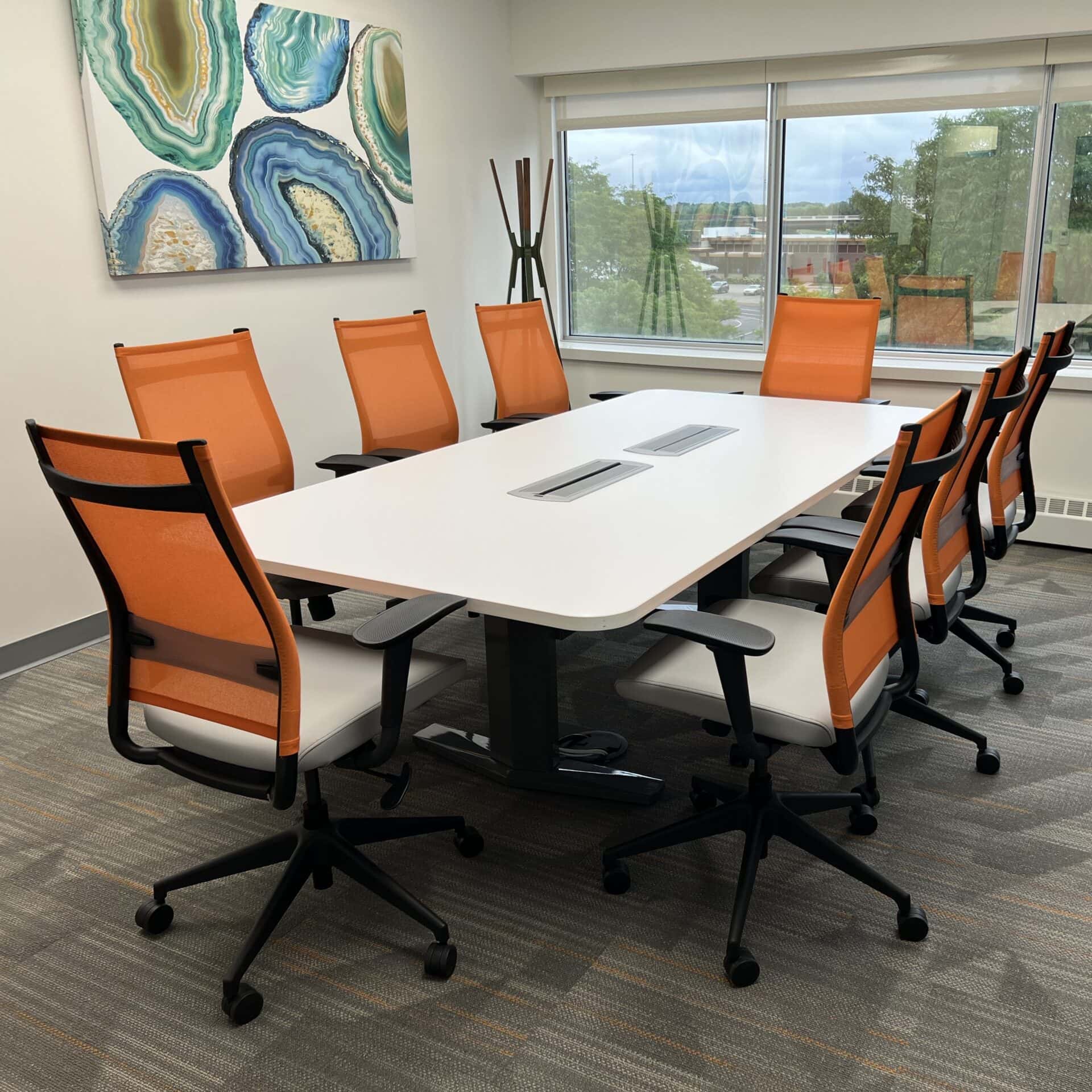 Modern office conference room with orange mesh chairs and white table for collaborative workspace.
