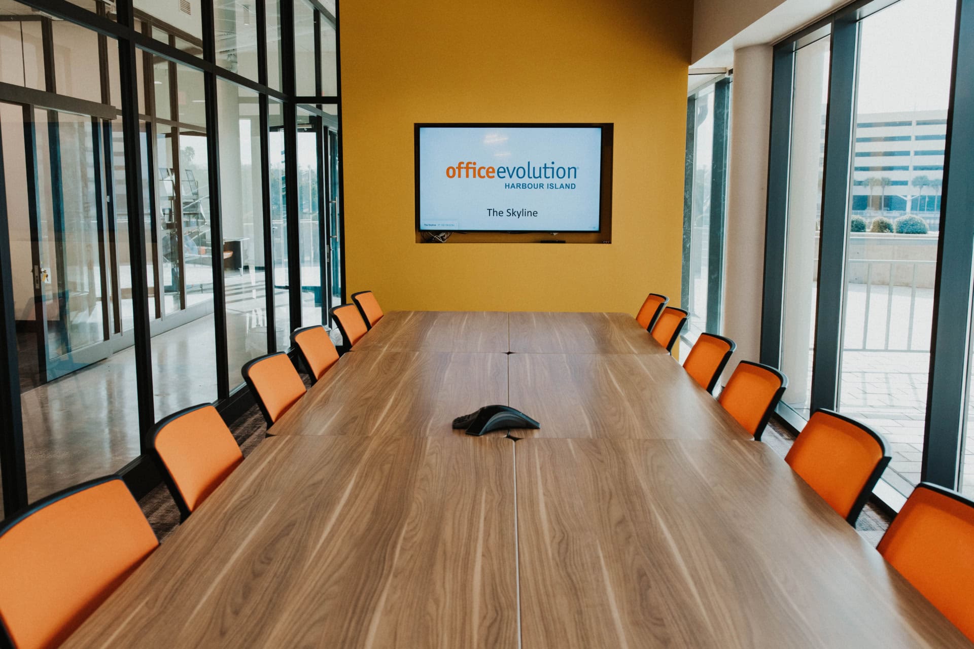 Modern conference room at Office Evolution with orange chairs and a large screen.