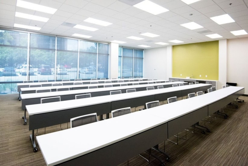 Modern conference room with long white tables and chairs, large windows, and a green accent wall.