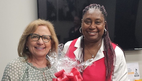 Two women smiling, one holding a gift with a red ribbon, at a professional event.