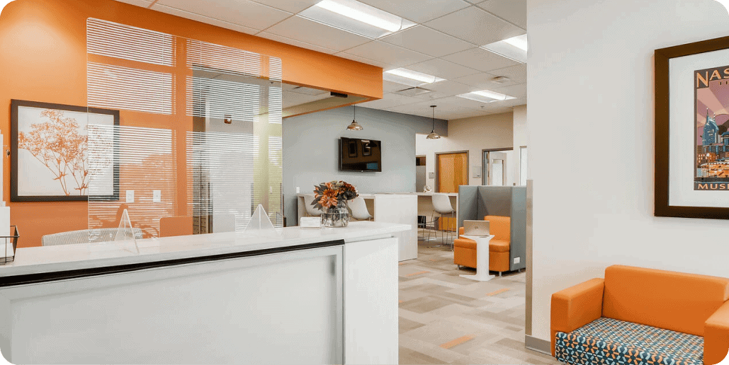 Modern office reception area with orange and gray accents and comfortable seating.