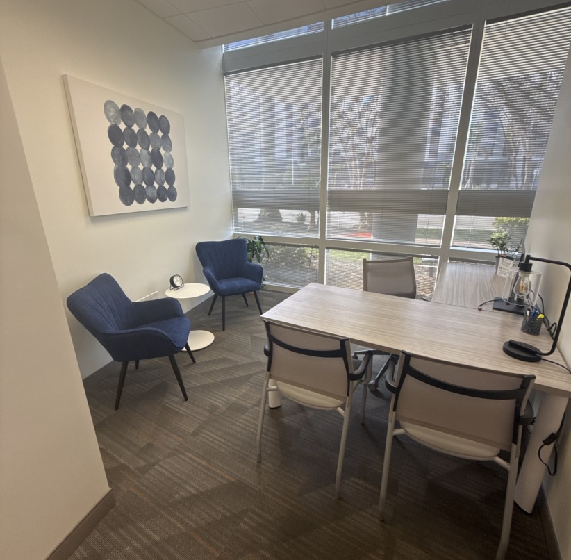 Modern office meeting room with large windows, blue chairs, and a wooden table.